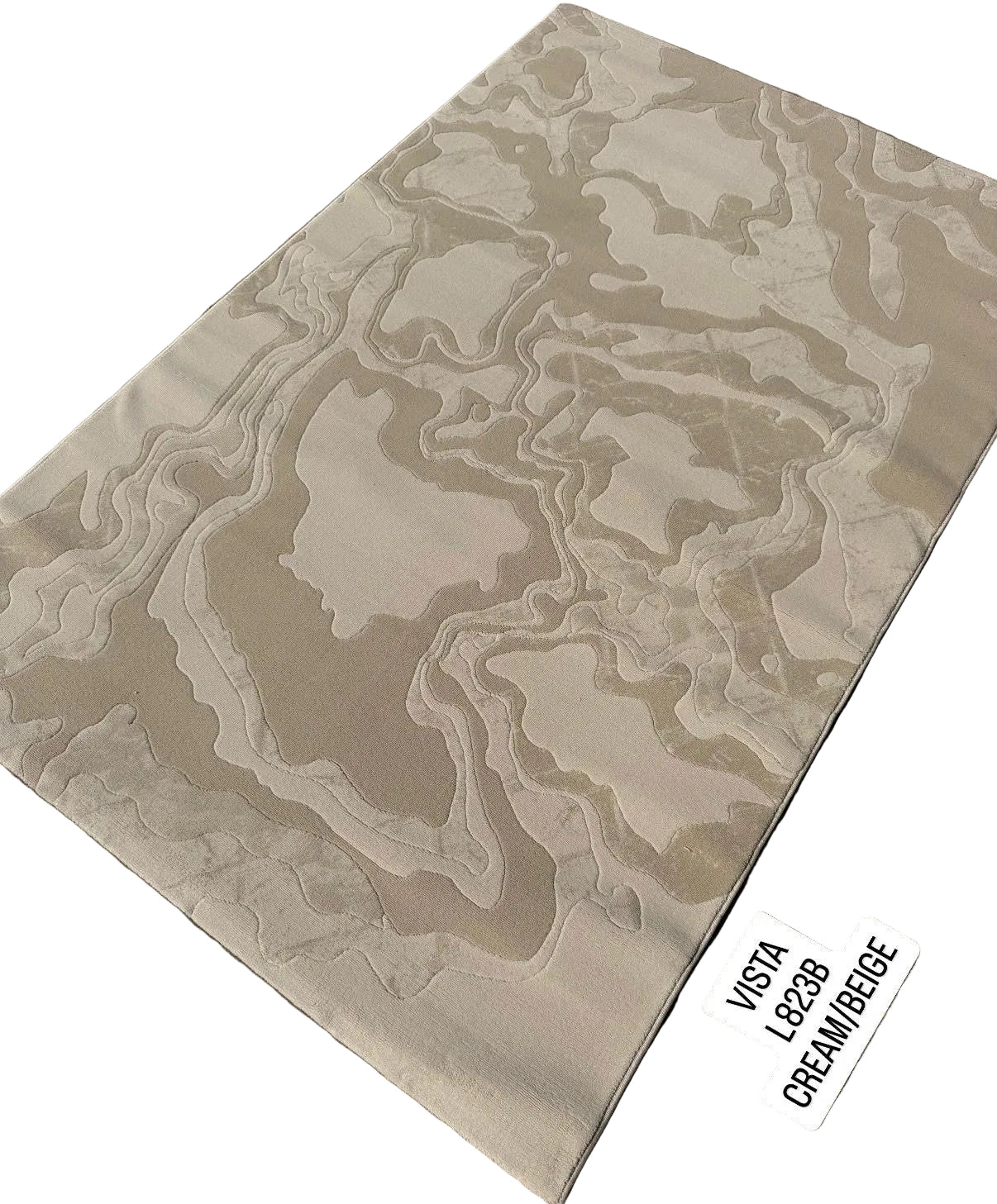 A rectangular area rug with an abstract, topographic contour pattern in cream and beige tones, displayed diagonally on a gray interlocking paver surface. A white label in the bottom right corner reads 'VASTI L828R CREAM/BEIGE'.